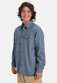 Blauwe geruite flanellen shirt met twee borstzakken en knoopsluiting aan de voorkant. Heeft lange mouwen en een relaxed fit. De textuur van de stof voegt diepte toe.