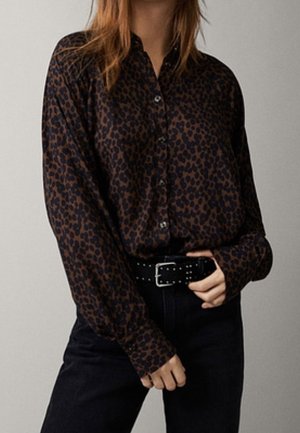 Camicia a maniche lunghe con stampa leopardata in marrone scuro e nero, vestibilità comoda, abbinata a una cintura nera con borchie e jeans scuri.