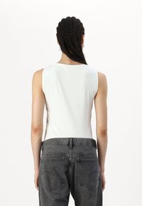 Débardeur blanc à côtes avec un col montant, associé à un jean taille haute gris foncé doté de deux poches arrière et d'un détail de couture subtil.