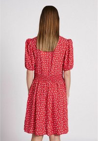 Rotes Floral-Kleid mit puffärmel, gerüschtem Taillenbund und knielanger Rocklänge. Mit kleinen weißen Blumenmustern auf einem strukturierten Stoff.