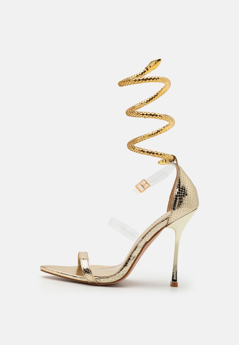 Zlaté vysoké sandály na podpatku s nárameníkem ve tvaru hada, texturovaným metalickým svrškem, průhlednými pásky a stiletto podpatkem.