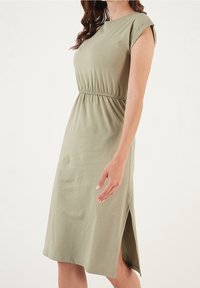Olivgröna klänning av jerseymaterial med korta ärmar, rynkad midja och sidoklyfta. Mjuk textur med en enkel, rak silhuett.