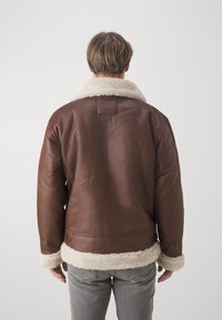 Giubbotto in pelle marrone con collo e polsini in pelliccia sintetica beige, caratterizzato da una texture liscia e un design aderente, visto dal retro.