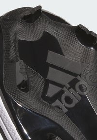 Crne nogometne kopačke s teksturiranim potplatom, trodimenzionalnim naglascima i crnim brendiranjem. Dizajn uključuje vidljive češljeve za prianjanje.