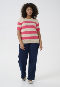 Gestreepte korte mouwen sweater in beige met felle roze strepen, gecombineerd met donkerblauwe wijde jeans en lichtgekleurde schoenen.