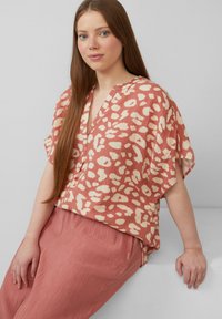 Lockere Kurzarm-Bluse in Koralle mit abstrakten cremfarbenen Mustern. V-Ausschnitt-Design kombiniert mit texturierten, passenden rosa Plisseehosen.