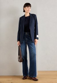 Navy pinstriped blazer, fitted black top, wide-leg blue jeans, brown leather handbag, and brown heeled shoes. Smooth, structured textures.