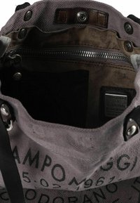 Canvas tas met een grijze buitenkant met zwarte letters, een bruine binnenkant, metalen beslag en meerdere sluitopties waaronder drukknopen en ritsen.