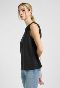 Sort ærmeløs top med en afslappet pasform, lavet af blødt stof, med en rund halsudskæring og sideslids, matchet med lyseblå denimjeans.