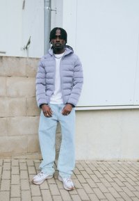 Lys lilla pufferjakke, hvid t-shirt, lyseblå løse jeans og grå-brune sneakers. Bemærkelsesværdige sølvringe og fletninger.