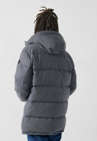 Giacca a vento grigia con cappuccio, caratterizzata da un design trapuntato, polsini elasticizzati e un logo sulla manica. Tessuto morbido e strutturato.