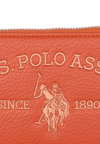 Portafoglio in pelle arancione con logo "U.S. Polo Assn." impresso e dettagli di cucitura, e un'illustrazione di una scena storica di polo. Chiusura a zip.