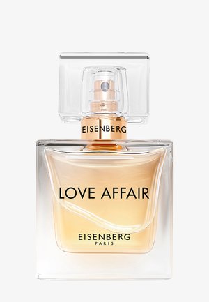 Klart glas parfume flaske med en facetteret kvadratisk kappe. Indeholder gylden væske, mærket "LOVE AFFAIR" og "EISENBERG PARIS" i fed sort skrift.