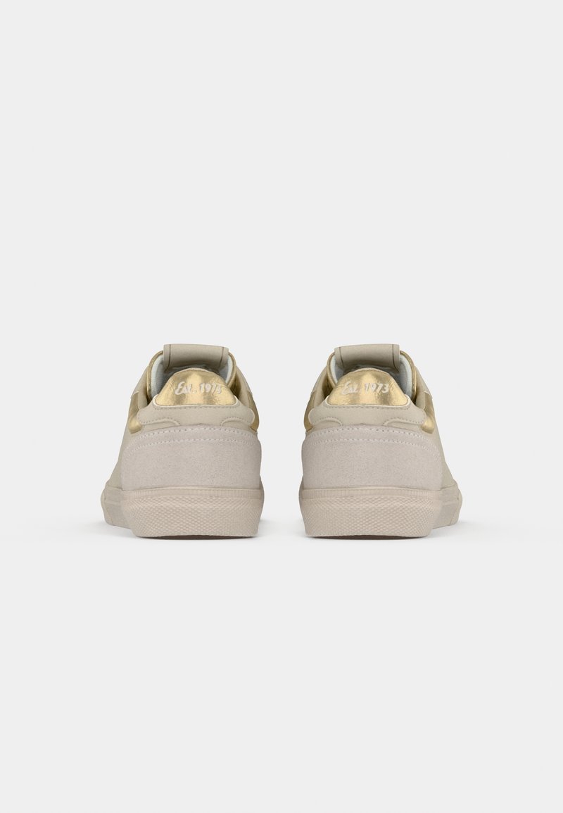 Zapatillas de ante beige con un acento dorado en el talón, que presentan una suela de goma texturizada y un cuello acolchado para mayor comodidad.
