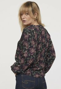 Blouse à manches longues en tissu sombre avec un motif floral violet et des feuilles vertes. Présente une coupe décontractée et un design à dos plissé.
