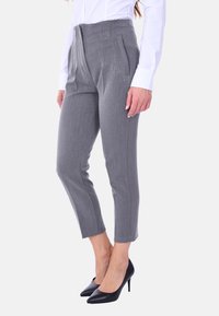 Pantaloni grigi su misura con una texture liscia, lunghezza cropped e tasche frontali, abbinati a scarpe con tacco nere a punta e una camicia bianca.