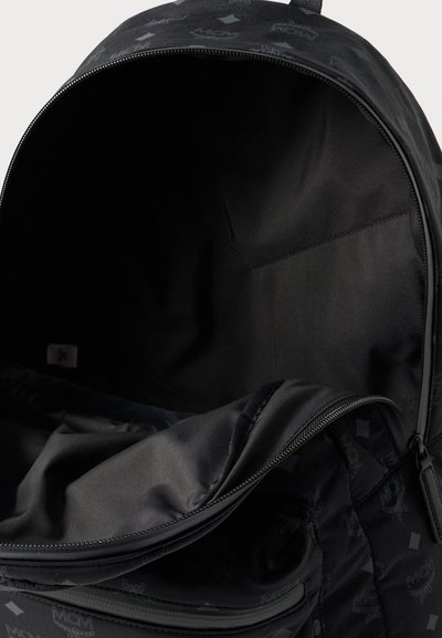Interior de mochila preta com textura lisa e mate. Inclui um compartimento principal com um bolso com fecho e um padrão sutil de logotipos.