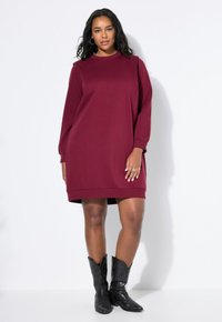 Vestido sudadera burdeos de Marlyn con mangas largas, cuello acanalado y dobladillo, combinado con botas de vaquero negras. Textura de tela suave.