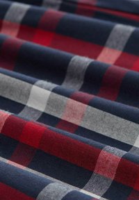 Tartan-Stoff mit rot, marineblau und weißen karrierten Mustern, der eine weiche Textur aufweist und in überlappenden Falten angeordnet ist.
