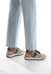 Sneaker con una combinazione di suede grigio e beige e pelle, caratterizzati da un accento con stampa leopardata sul tallone e un design con lacci neri.