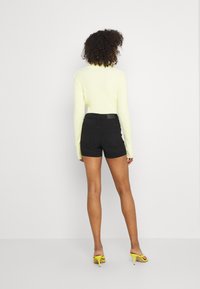 Pantalones cortos de mezclilla negra con un diseño ajustado, combinados con un suéter de canalé amarillo brillante. Los accesorios incluyen sandalias de tacón amarillo.