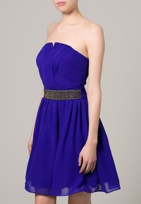 Šaty bez ramínek v purpurové barvě se skládanou korzetovou částí, hladkou sukní a korálkovým páskem v pase, které zdůrazňují jemnou, lehce splývavou strukturu.
