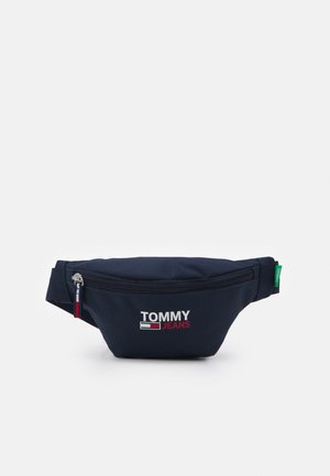 Granatowa torba na pas z przednią kieszenią na zamek, logo "Tommy Jeans" w białym i czerwonym kolorze oraz regulowany pasek z zieloną metką.