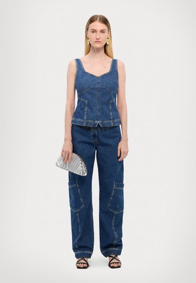 Débardeur en denim avec un col carré, associé à un pantalon en denim loose avec de grandes poches. Accessoirisé avec une pochette en argent.