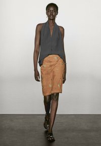 Haut à bretelles gris associé à une jupe en suède beige ornée de broderies d'étoiles dorées, complété par des sandales noires. Textures lisses et coupe ajustée.