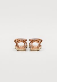 Sandales ouvertes avec des sangles transparentes, des accents or rose et des semelles en jute tressé. Présente des clous décoratifs le long des sangles.