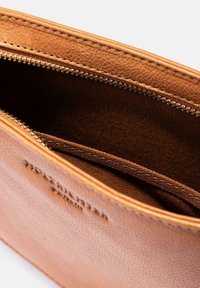 Braune Ledertasche mit strukturiertem Äußeren und einem goldenen Reißverschluss, der ein glattes Innenfutter in einem ähnlichen Braunton enthüllt.