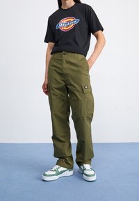 Czarny, graficzny t-shirt z logo "Dickies", zestawiony z oliwkowozielonymi spodniami cargo z bocznymi kieszeniami oraz białozielonymi sneakersami.
