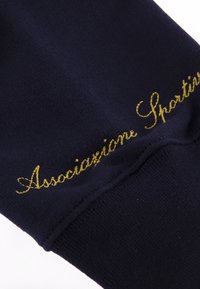 Marineblauwe stof met een gladde textuur, voorzien van gouden geborduurde tekst "Associazione Sportiva" nabij de rand.