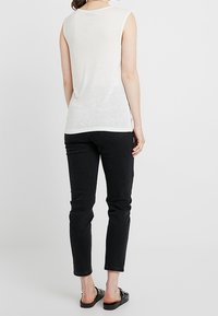 Top bianco senza maniche con una vestibilità rilassata, abbinato a jeans neri slim-fit. Dettagli notevoli includono orlo arrotolato e sandali piatti.