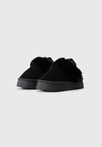 Schwarze Wildleder Slipper mit einem flauschigen schwarzen Kunstfell-Akzent, dicker Sohle und strapazierfähigem Gummiprofil für guten Halt. Lässiges und gemütliches Design.