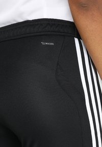 Black athletic pants with Climalcool branding. Features include white stripes and a textured fabric, suitable for active wear.