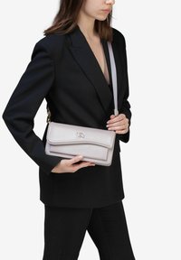 Lyse lilla læder håndtaske med klaffelukning og guldfarvet hardware, båret på tværs af kroppen med en tynd justerbar rem.