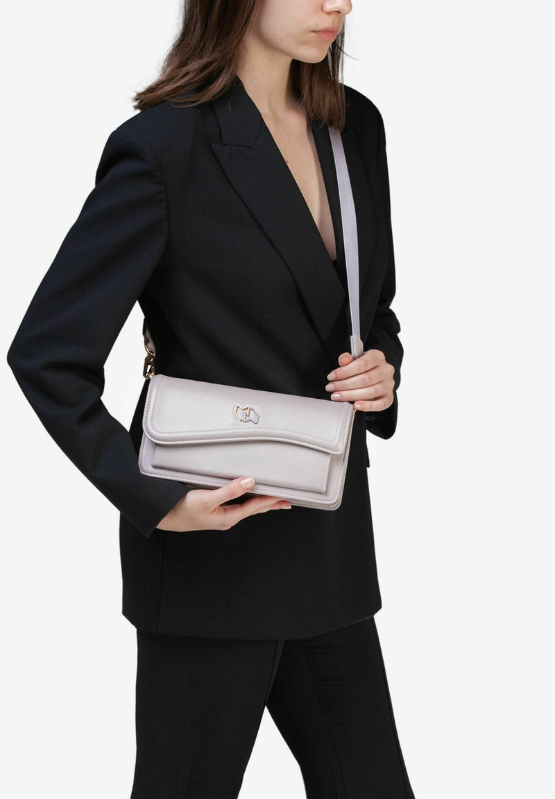 Lyse lilla læder håndtaske med klaffelukning og guldfarvet hardware, båret på tværs af kroppen med en tynd justerbar rem.