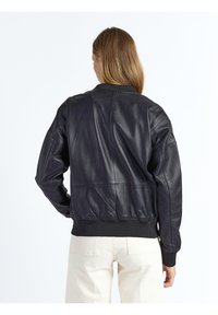 Zwarte leren bomberjack met geribbelde manchetten en zoom. Heeft een gladde textuur en een relaxte pasvorm met een strak ontwerp.