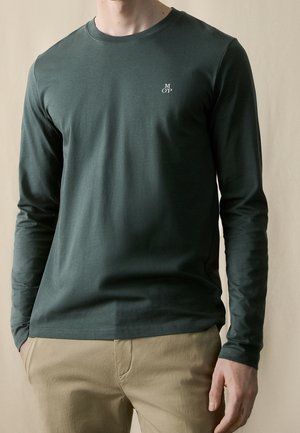 Donkergroene longsleeve t-shirt met een ronde hals en subtiele logo-detail op de borst. Zacht, ademend materiaal met een gladde textuur.