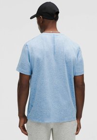 Light blue short-sleeve t-shirt with a subtle texture, round neckline, and a vertical seam detail on the back. Paired with gray pants.