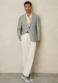 Sacou personalizat gri deschis peste o cămașă crem cu un model texturat, asortat cu pantaloni crem și adidași verde deschis.