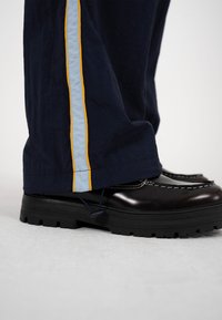 Juodi batai su stambiu padu derinami su tamsiai mėlynomis kelnėmis, kurių šone eina vertikali mėlyna juosta, apjuosta plonomis geltonomis linijomis.