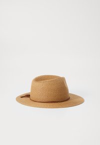 Sombrero de paja tejido en marrón claro con un ala ancha. Presenta una banda marrón alrededor de la base y un pequeño lazo decorativo a un lado.