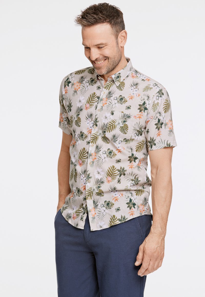 Camisa de manga corta con botones en tela ligera, con un patrón floral y de hojas en verde, naranja y blanco sobre un fondo beige.
