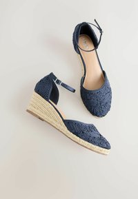 Chaussures compensées espadrilles bleu marine avec empeignes en tissu brodé et brides à la cheville, dotées de talons enveloppés de jute et de semelles intérieures beiges.