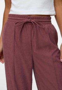 Pantalon en velours côtelé d'un mauve profond avec une taille élastique, un cordon de serrage à l'avant et des plis verticaux sur les côtés, mettant en valeur une texture douce.
