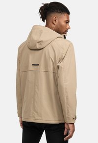 Beige, lichte jas met capuchon, voorzien van een ventilatie detail op de rug en knoop manchetten. Gladde textuur en minimalistisch ontwerp.