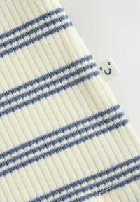 Tkanina z črtami v kremni in mornarsko modri barvi, z rebrasto teksturo in majhno etiketo z nasmejanim obrazom na robu.