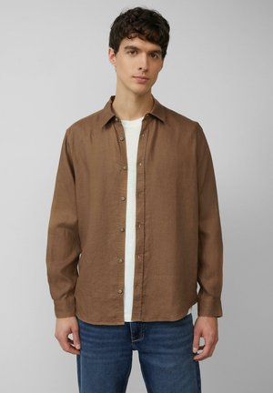 Braunes Leinenhemd mit langen Ärmeln und Button-Down-Kragen, mit einer Knopfleiste und Knopfdetails, über einem weißen Hemd getragen.